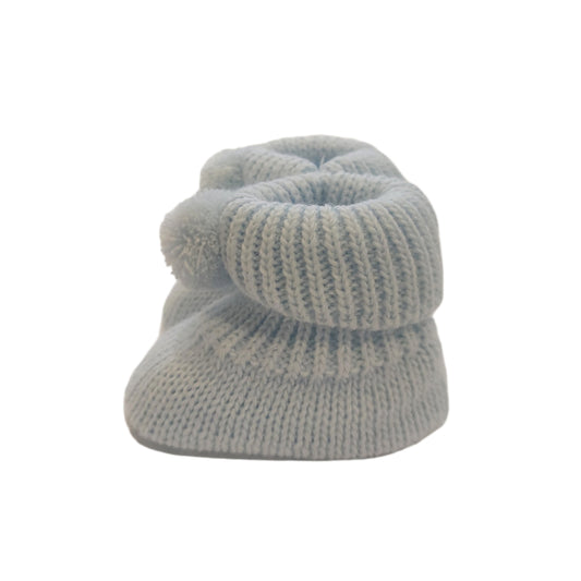 Side view of a blue Nursery Time knitted baby bootie on a white background, showing the ribbed cuff, pom-pom detail and textured knitted foot.