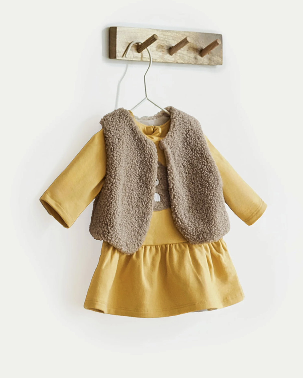 Mayoral girls Yellow dress with brown fur vest outfit set hanging on a wooden hook. BABY GIRL TEDDY DRESS, GILET & HEADBAND SET - SAFFRON YELLOW | MAYORAL