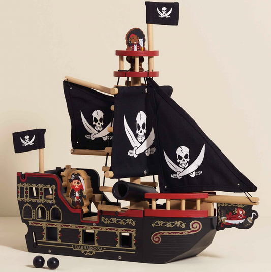 Pirate ship model with black sails and skull flags on a beige background BARBAROSSA WOODEN PIRATE SHIP & CHARACTERS | LE TOY VAN