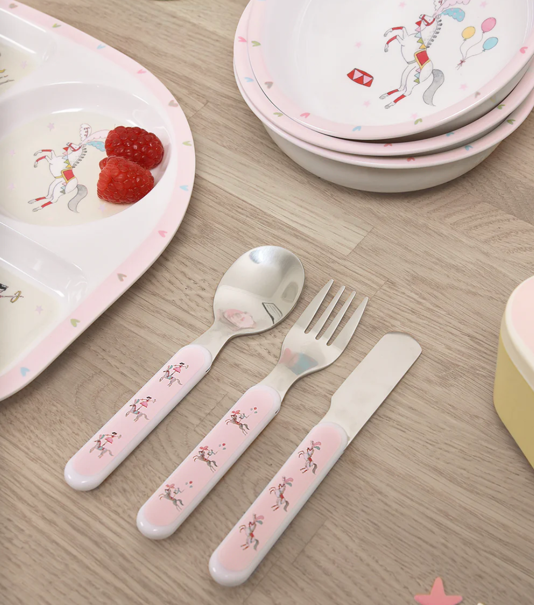 Children's tableware set with pink handles including a spoon, fork, and knife on a wooden surface. CHILDREN'S MELAMINE CUTLERY SET - FAIRGROUND PONIES | SOPHIE ALLPORT