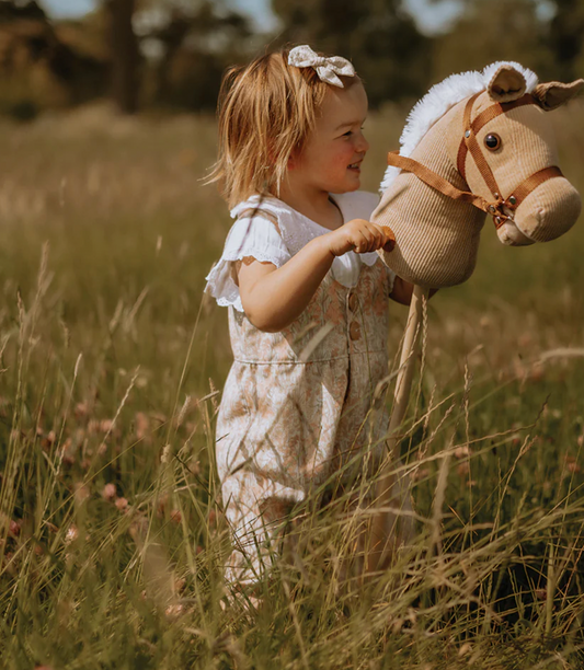 Child holding a plush horse toy in a grassy field. CLASSIC CHILDREN'S CORD HOBBY HORSE | BIGJIGS
