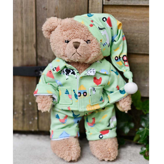 A teddy bear wearing a green farmyard print pyjama set with a matching sewn-on nightcap, featuring colorful animal and farm elements. CUDDLY TEDDY IN FARMYARD PYJAMAS | POWELL CRAFT