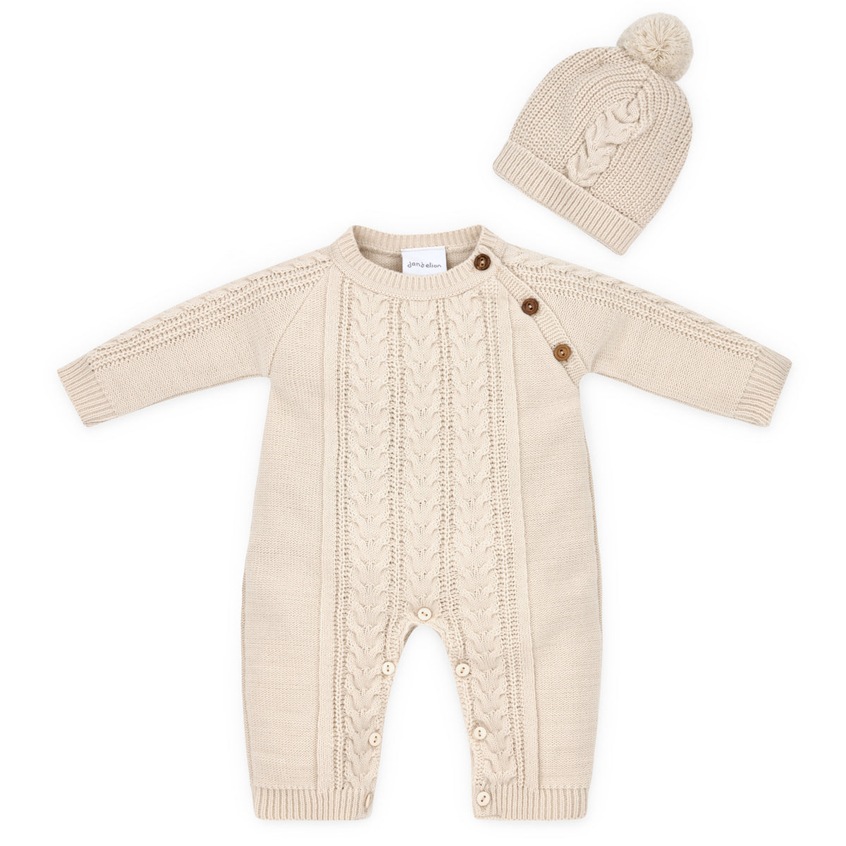 Dandelion Knitted Cable Knit Baby Onesie and Hat Set in Neutral Taupe shown as a flat lay on a white background; full-length onesie in warm oat-taupe acrylic knit with a central cable-knit panel running from chest to ankle flanked by moss-stitch side panels; three round wooden buttons at the right shoulder; Dandelion woven label at the neckline; ribbed cuffs at wrists and ankles with inner leg wooden button fastenings; matching close-fitting cable-knit beanie with a small pompom at the crown
