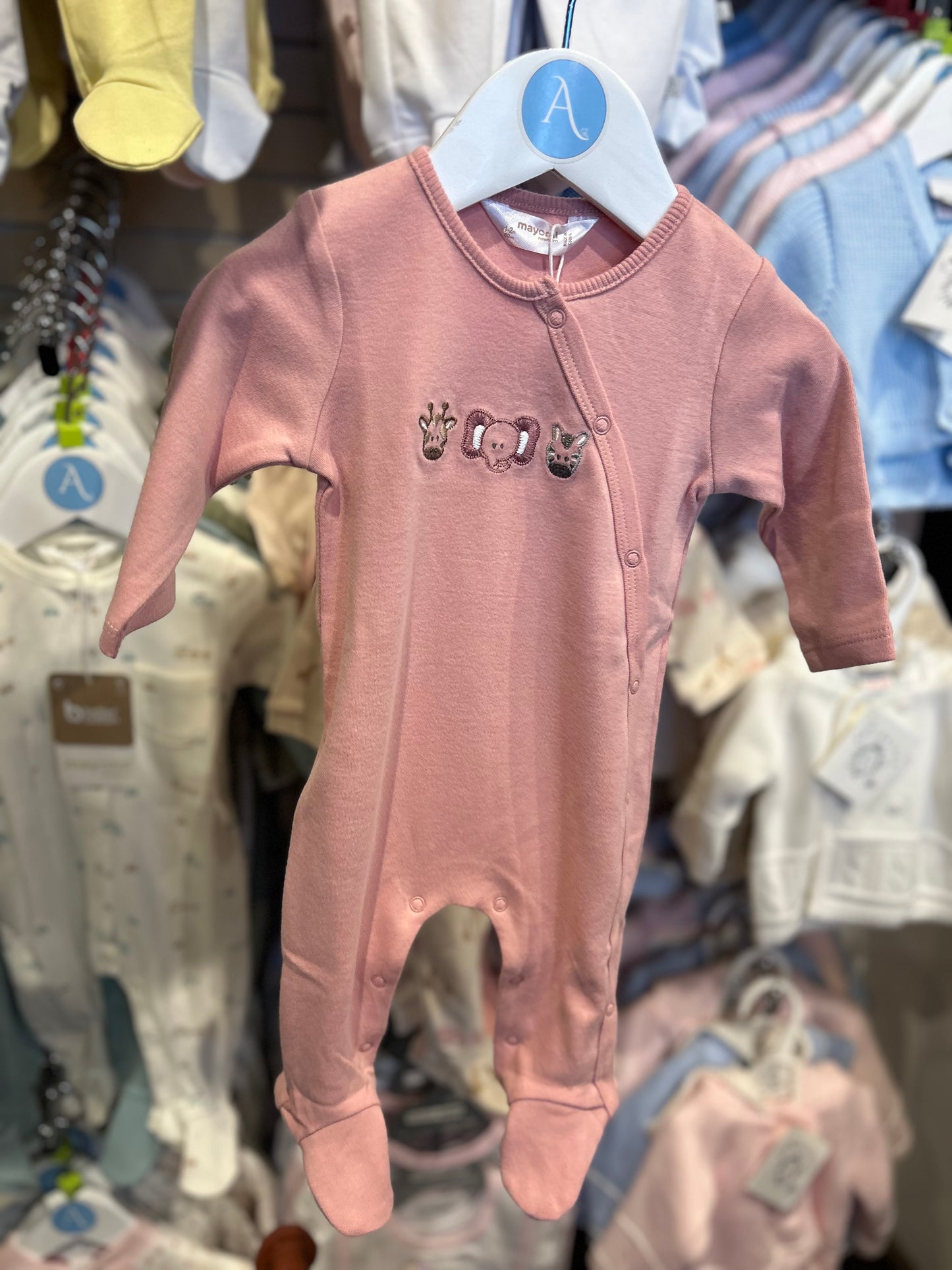 Pink baby onesie with designs on a hanger against a background of other baby clothes. MAYORAL BABY COTTON SLEEPSUIT - PINK JUNGLE FACES