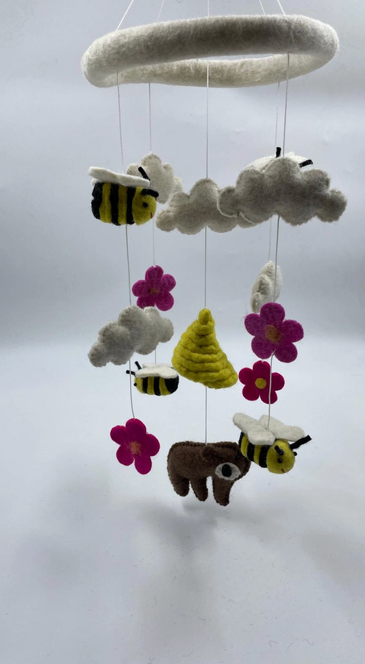 Funky Yak handmade needle-felted bears and bees nursery cot mobile — close-up three-quarter view showing the white felt ring hoop and the detail of the three bees with yellow-and-black stripes and white wings, the brown bear with white wings, the golden beehive, grey-white clouds and hot pink daisy flowers with yellow centres