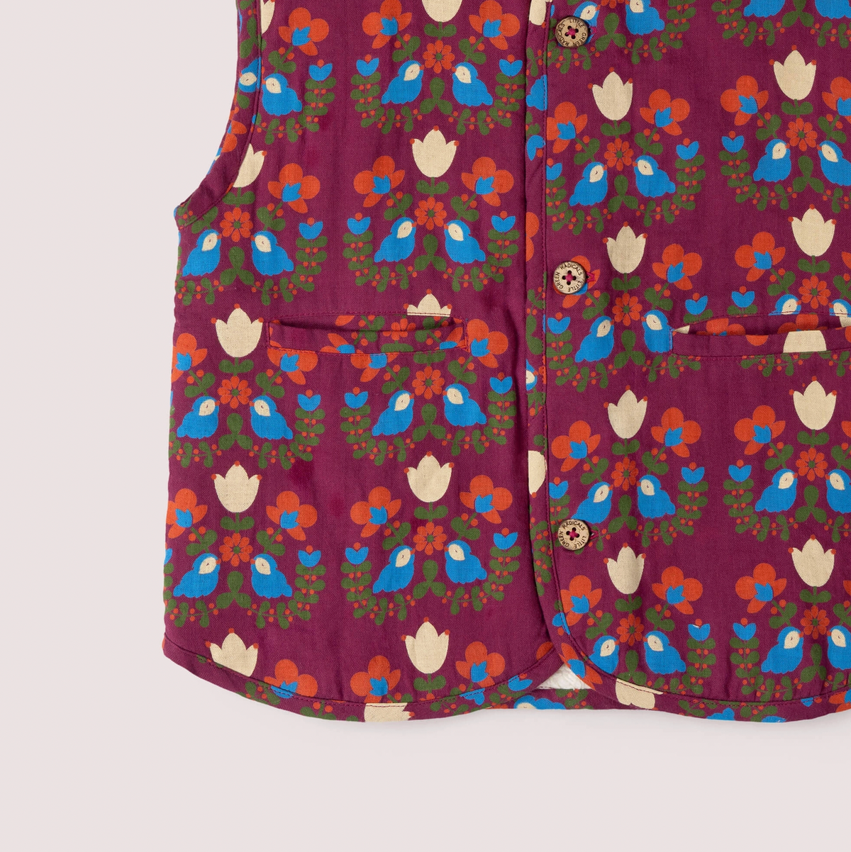 Little Green Rascals Folk Birds reversible gilet — close-up of the lower print side showing the two patch pockets with cream tulip motifs, branded coconut shell buttons and the folk art print detail of blue birds, cream tulips, orange flowers and olive green foliage on burgundy
