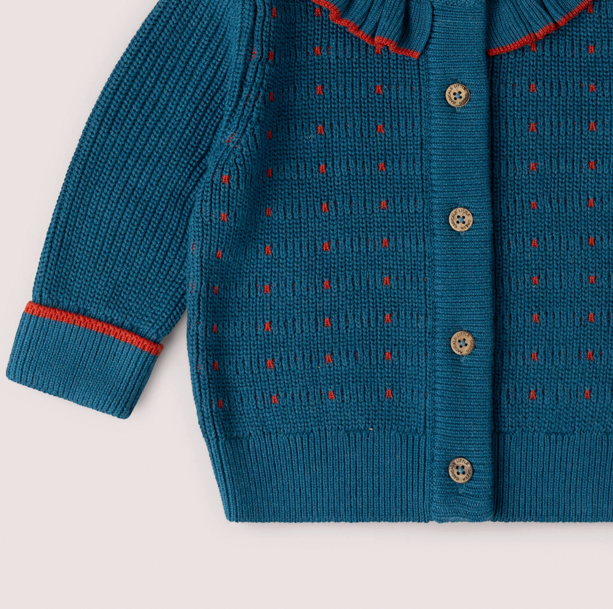 Little Green Rascals Midnight Frill Snuggly Cardigan — close-up of the lower body and cuff showing the scattered red dash stitch pattern throughout the midnight teal chunky knit, branded coconut shell buttons down the front placket, and ribbed turned-up cuff with red contrast stripe