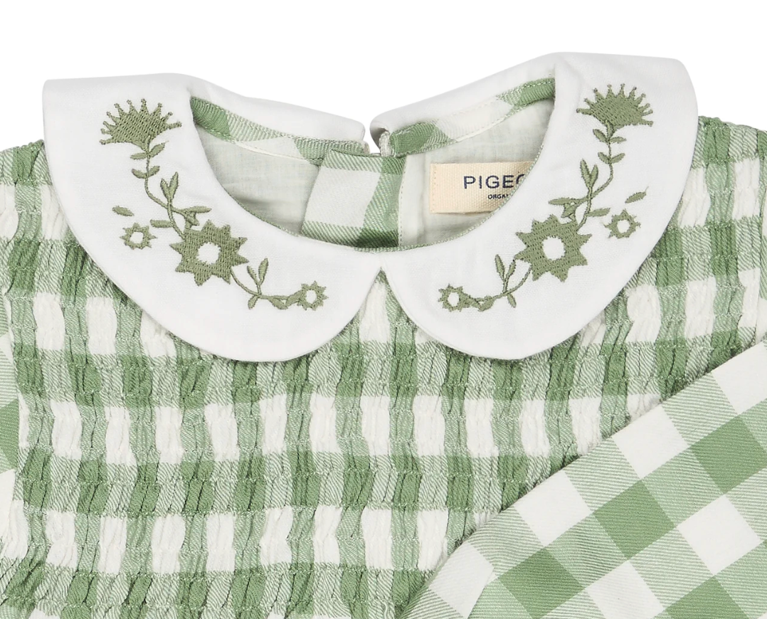 Close-up — tonal sage embroidery in sharp focus; Pigeon Organics label clearly visible; smocking construction; woven fabric texture; back neck opening.