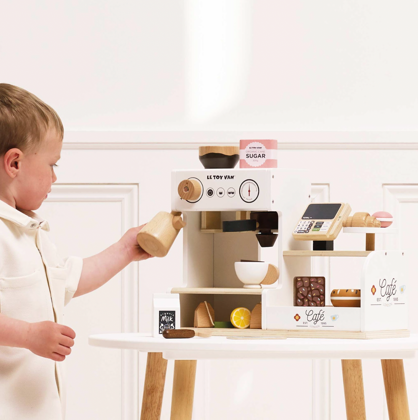 Child playing with a toy coffee set on a white surface. WOODEN BARISTA CAFE SHOP | LE TOY VAN