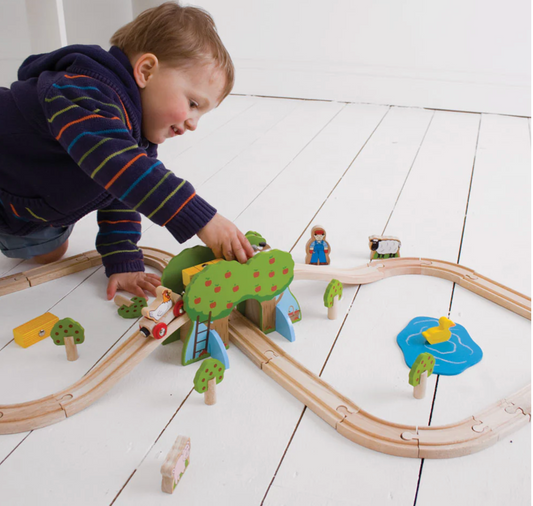 Child playing with a wooden toy train set on a white floor WOODEN FARM TRAIN SET | BIGJIGS