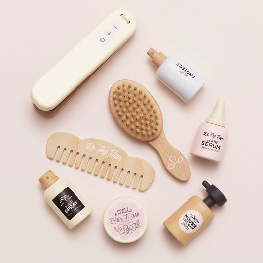 Collection of hair care products including bottles, a brush, and combs on a light pink background. WOODEN HAIR STRAIGHTENERS & ACCESSORIES SET | LE TOY VAN