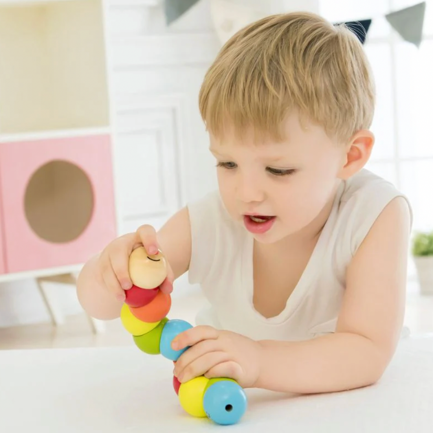 Child playing with a colorful wooden toy in a bright room. WOODEN TWISTY CATERPILLAR | CLASSIC WORLD