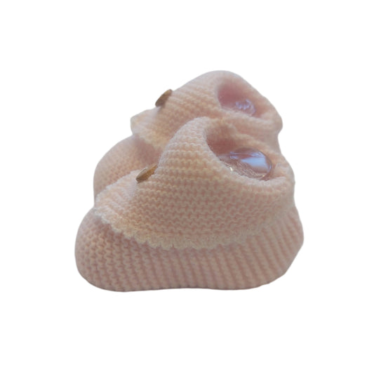 Pink crochet-knit baby booties shown from a low side angle on a white background; the ribbed ankle cuff, textured knit body, scalloped flap and button detail are visible