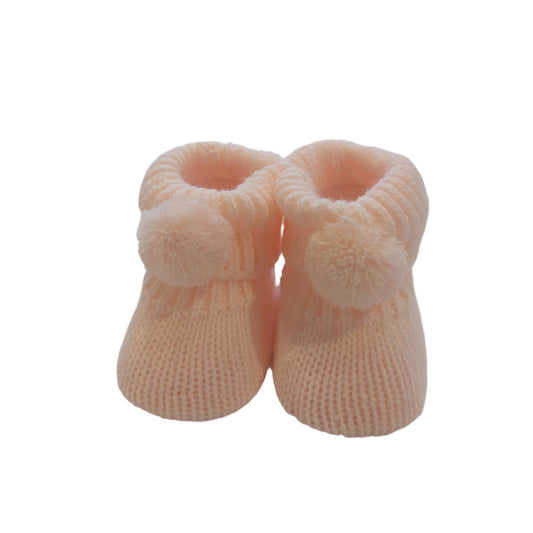 Pair of pale pink Nursery Time knitted baby booties on a white background, showing matching pom-poms, ribbed cuffs and textured knitted uppers.