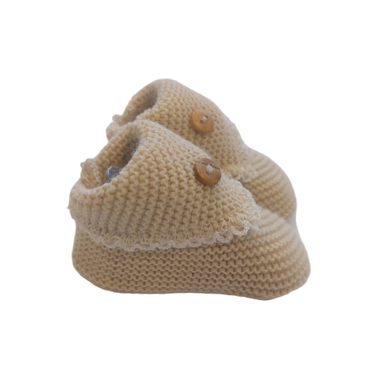 Beige crochet-knit baby booties shown from a side angle on a white background; the rounded toes, ribbed ankle cuffs, textured knit and buttoned flaps are visible