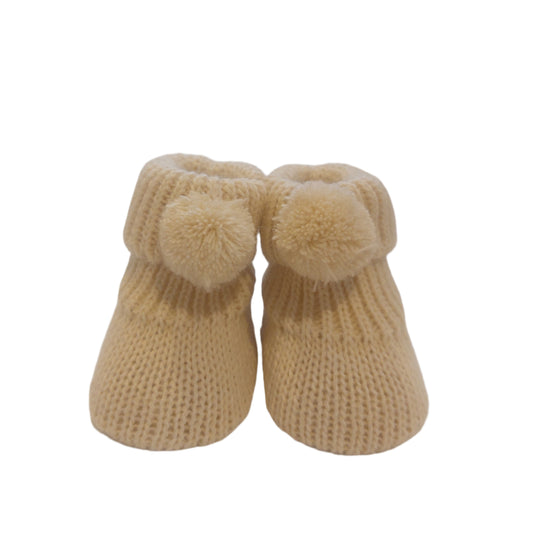 Side view of a blue Nursery Time knitted baby bootie on a white background, showing the ribbed cuff, pom-pom detail and textured knitted foot.