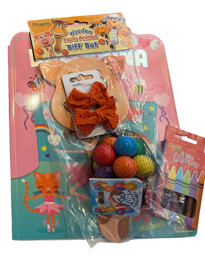 Two packaged children's gift sets displayed side by side on a white surface against a wooden tabletop. Each set contains pink and teal carded packaging with cartoon cat graphics and includes items such as a ballerina-themed box, biff bat toys, crayons, and small accessories.