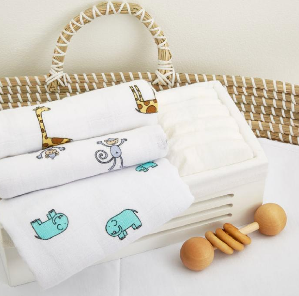 Set of baby towels with animal prints in a basket with a wooden rattle on a white background. ADEN + ANAIS 3 PACK COTTON BABY MUSLIN SQUARES - JUNGLE JAM