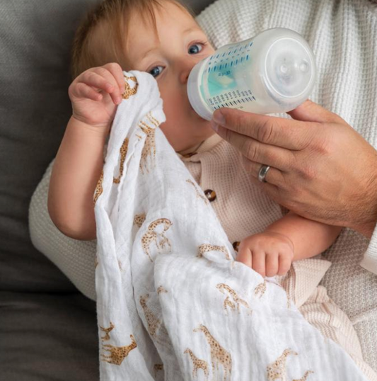 Baby being bottle-fed with a white blanket with animal patterns. ADEN + ANAIS 3 PACK ORGANIC COTTON BABY MUSLIN SQUARES - SAFARI DREAMS