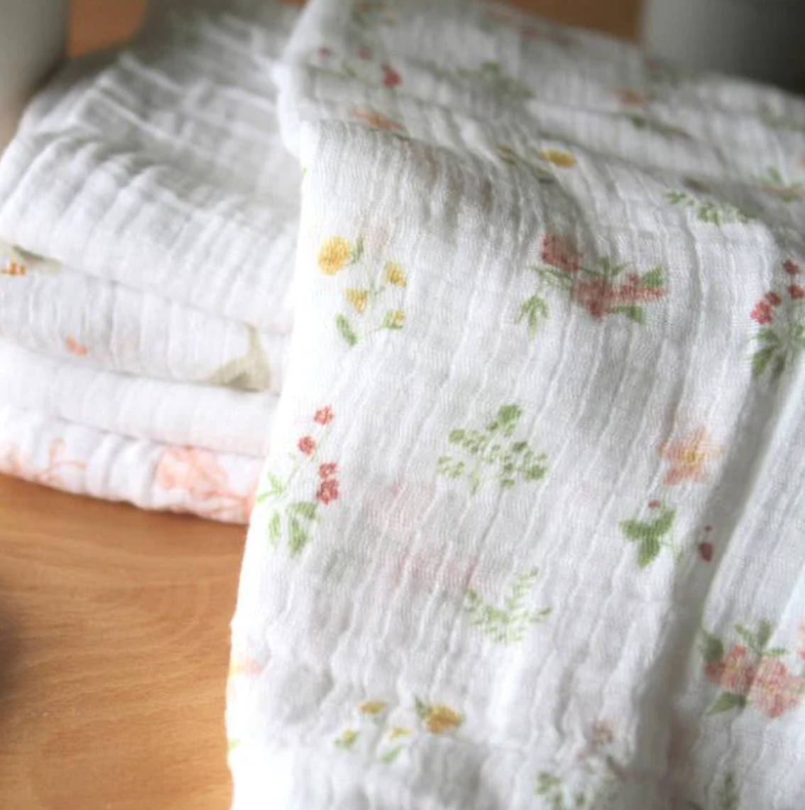 Stack of white muslin cloths with floral patterns on a wooden surface. ADEN + ANAIS 5 PACK BABY MUSLIN SQUARES - COUNTRY FLORAL