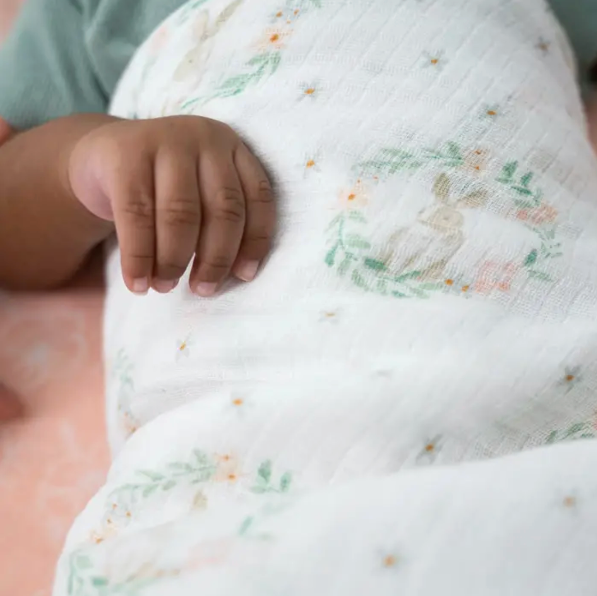 Close-up of a baby's hand holding a soft, textured blanket. ADEN + ANAIS COTTON BABY SWADDLE 4 PACK - BLUSHING BUNNIES