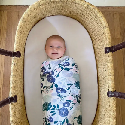 Baby swaddled in a floral blanket lying in a moses basket. ADEN + ANAIS COTTON BABY SWADDLE 4 PACK - FLOWERS BLOOM