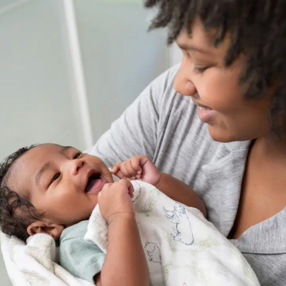 Woman holding a baby wrapped in a blanket, both looking at each other. ADEN + ANAIS COTTON BABY SWADDLE 4 PACK - HARMONY