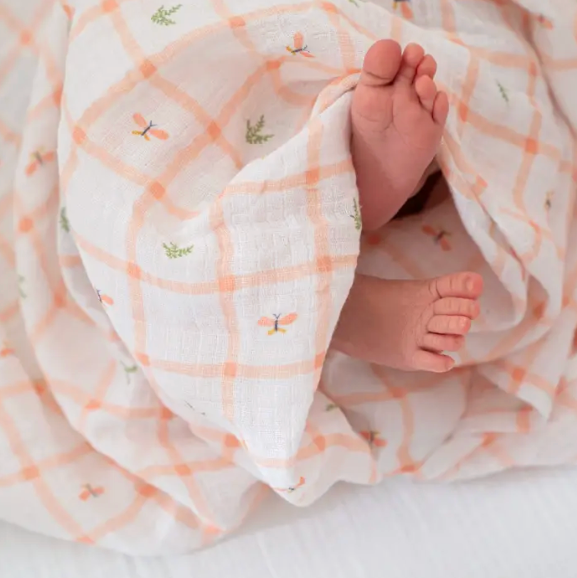 Baby feet peeking out from under a soft, patterned blanket. ADEN + ANAIS COTTON SWADDLE 4 PACK - COUNTRY FLORAL