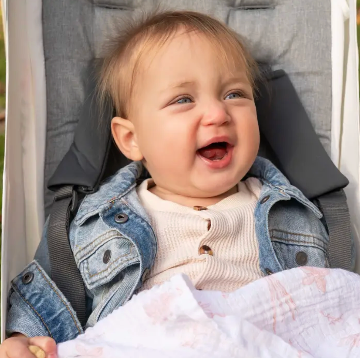Baby in a stroller wearing a denim jacket and smiling. ADEN + ANAIS COTTON SWADDLE 4 PACK - COUNTRY FLORAL