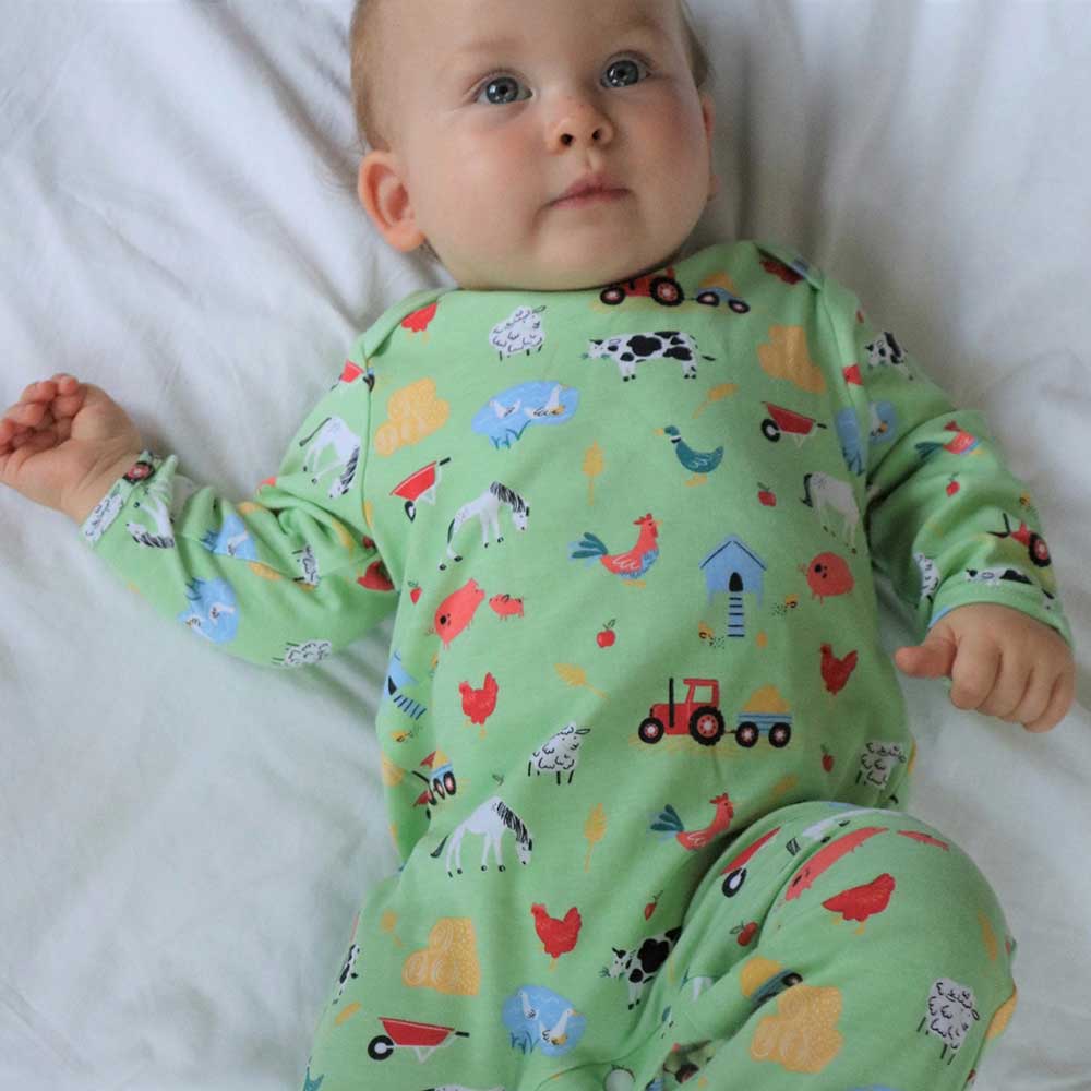 Baby wearing a green pajama with animal prints. BABY COTTON FARMYARD PRINT SLEEPSUIT WITH FEET | POWELL CRAFT