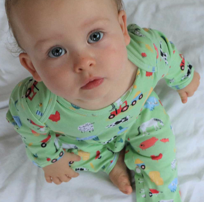 Baby wearing a green outfit with colorful patterns. BABY COTTON FOOTLESS FARMYARD SLEEPSUIT WITH POPPERS | POWELL CRAFT 