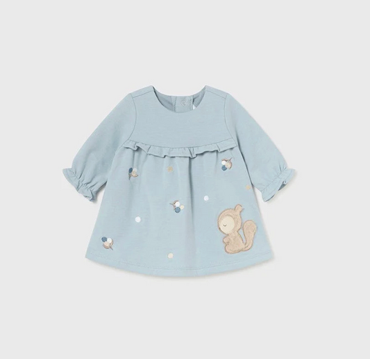Mayoral baby girls polar blue fleece squirrel dress — front flat lay on grey background showing soft polar blue A-line fleece dress with gathered yoke and double ruffle trim across the chest, long sleeves with elasticated ruffle cuffs, snap button at the back neck, scattered embroidered acorns and leaves in navy, grey and gold thread across the skirt, and large 3D sandy bouclé squirrel appliqué on the lower right skirt with embroidered face and fluffy tail