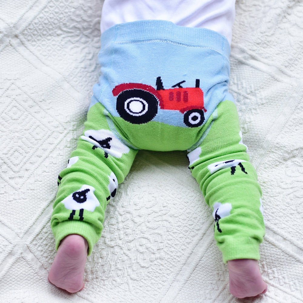 A pair of green leggings with a farm-themed design, including a red tractor on the knee area and a depiction of white sheep on the calf area, paired with a blue waistband. BABY TRACTOR & SHEEP LEGGINGS - 3 SIZES | POWELL CRAFT