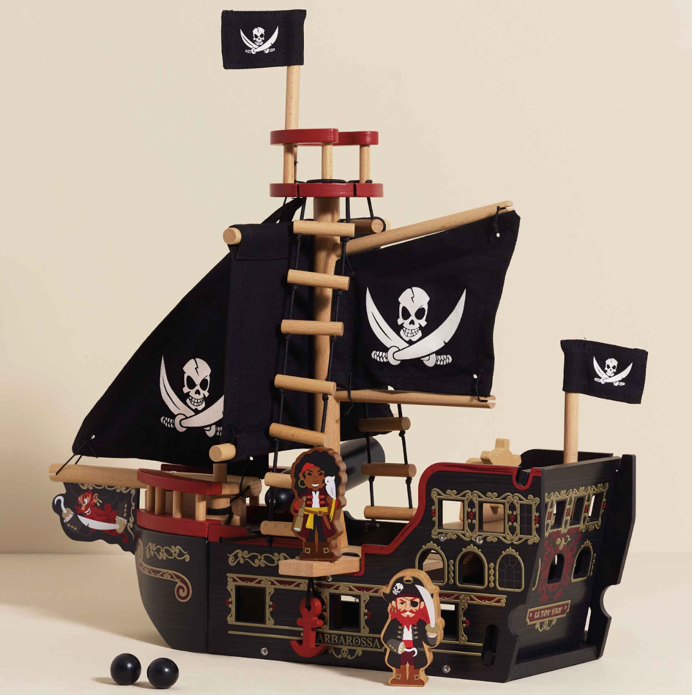 Toy pirate ship with flags and figures on a beige background BARBAROSSA WOODEN PIRATE SHIP & CHARACTERS | LE TOY VAN 