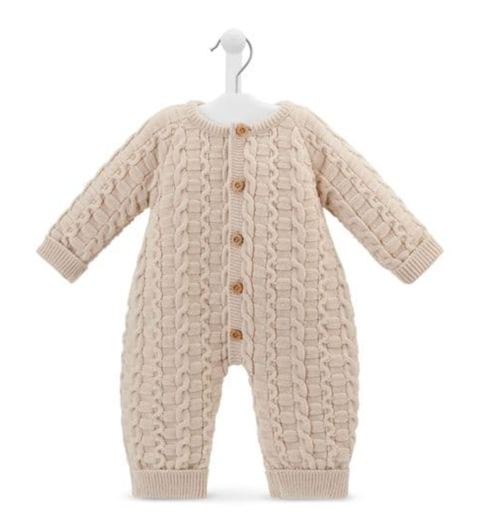 Dandelion basket weave knitted baby onesie in warm oatmeal taupe on a white hanger against a white background; full front view of a footless all-in-one with long sleeves and long legs; three-dimensional knit combining interlocking basket weave oval loop panels on the body and sleeves with twisted rope cable columns running vertically down the centre front and sides; five round gold-toned buttons down the centre front placket; round neckline with narrow ribbed neckband; ribbed cuffs at sleeve ends andbuttons