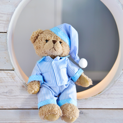 Teddy bear in blue pajamas sitting on a wooden surface with a mirror. BLUE_STRIPE_PYJAMAS_TEDDY_BEAR_SOFT_CUDDLY_TOY_IN_BLUE_NIGHTWEAR