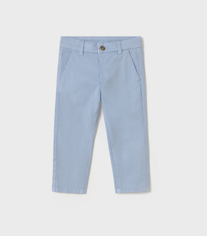 Mayoral Boys Basic Baby Blue Chino Trousers — front ghost flat-lay on light grey background; powder/pale blue cotton-elastane chino-style trousers; flat front with a pressed centre crease on each leg; concealed zip fly with a single small round antique/brass-tone metal button at the waistband clearly visible; belt loops at the waistband; two angled diagonal slash pockets at the front; plain straight-cut leg tapering slightly to a plain hemline at the ankle; light grey background; demonstrates the full front