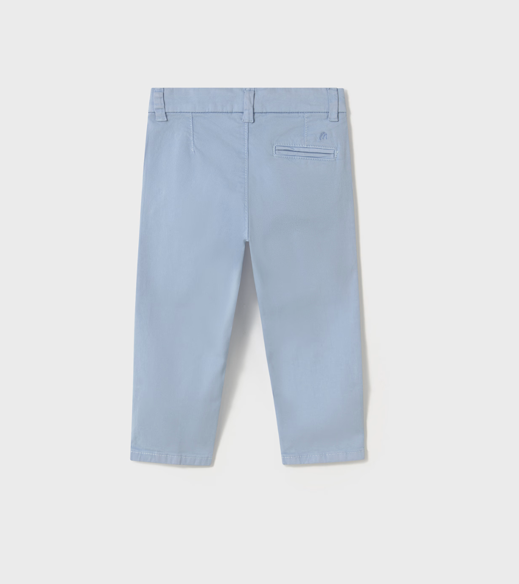 Mayoral Boys Basic Baby Blue Chino Trousers — back ghost flat-lay on light grey background; powder/pale blue cotton-elastane chino-style trousers viewed from behind; belt loops at the waistband including a centre back belt loop; single welt/jetted pocket on the right back hip with a small tonal embroidered Mayoral stylised M logo visible just to the right of the pocket opening; plain left back hip with no pocket; plain straight-cut leg tapering slightly to a plain hemline at the ankle; light grey background
