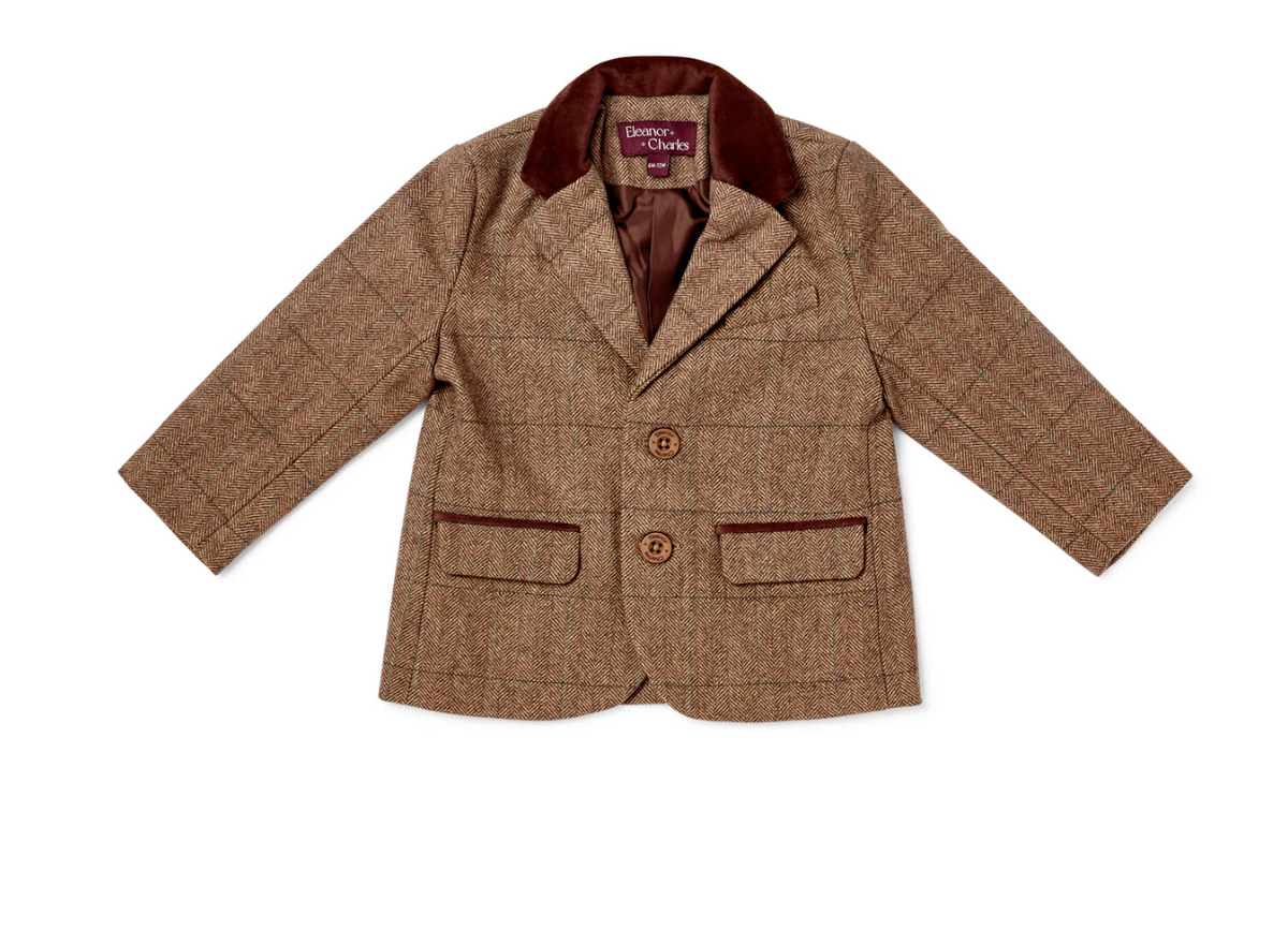 Eleanor Charles Boys Moloney Tweed Jacket in Brown trim colourway photographed flat lay from the front; tailored children's jacket in warm caramel-brown herringbone tweed; deep chocolate brown velvet notched lapel collar; two branded Eleanor Charles horn buttons in dark brown on the front button placket; two lower flap pockets with deep chocolate brown velvet contrast piping along the lower pocket flap edges; purple Eleanor Charles woven brand label at the inner collar neckline