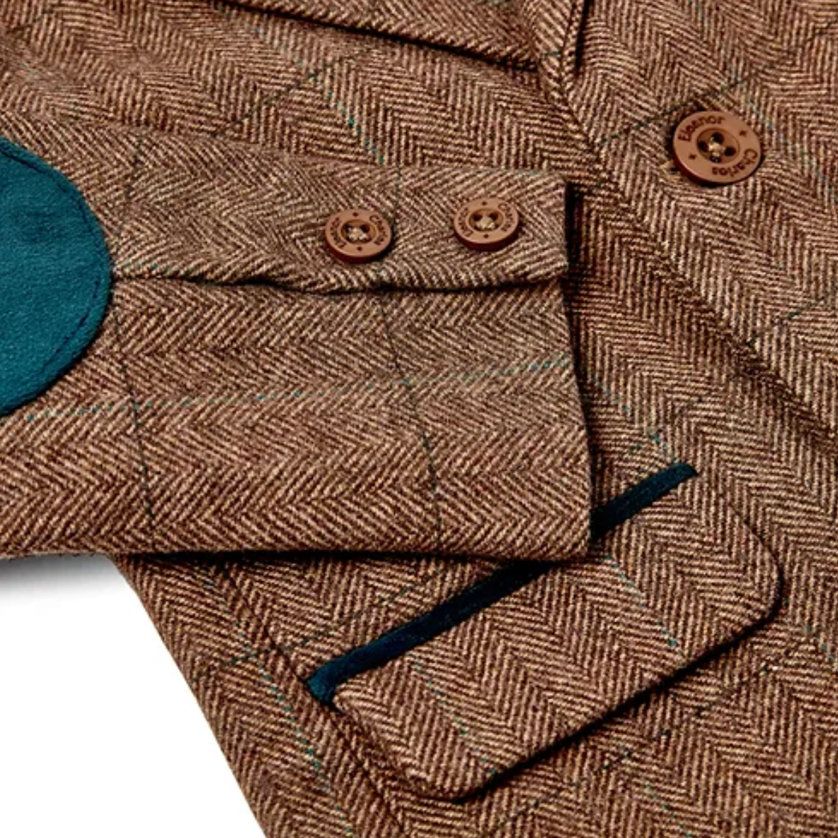 Close-up detail showing the right sleeve elbow patch, cuff buttons and lower pocket; large rounded oval peacock teal-blue velvet elbow patch at mid-sleeve; two small round branded Eleanor Charles horn cuff buttons on the sleeve cuff placket with fine Eleanor Charles text engraved around the rim; peacock teal-blue velvet contrast piping along the lower edge of the pocket flap; the herringbone tweed weave clearly visible — tight fine diagonal caramel and warm brown herringbone pattern with a subtle windowpane