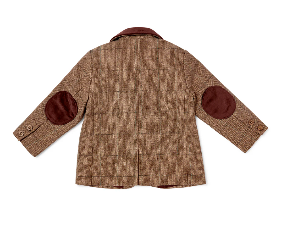 Eleanor Charles Boys Moloney Tweed Jacket in Brown trim colourway photographed flat lay from the back; warm caramel-brown herringbone tweed with a subtle windowpane overcheck clearly visible — fine darker windowpane lines crossing the herringbone ground at regular intervals; deep chocolate brown velvet notched collar at the top; two rounded oval chocolate brown velvet elbow patches on both sleeves at mid-sleeve; two small Eleanor Charles horn cuff buttons per sleeve; centre back vent at the lower hem; warm 