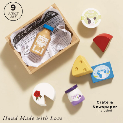 Set of toy food items including a bottle, cheese, and other shapes with a crate and newspaper in the background. CHEESE & DAIRY WOODEN TOY MARKET CRATE | LE TOY VAN
