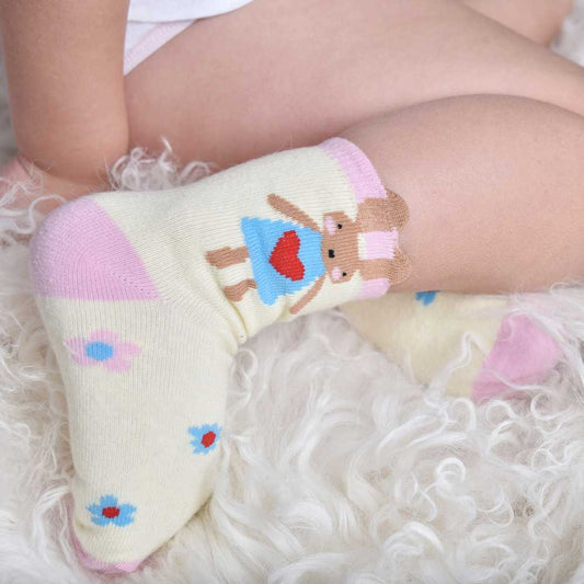 A pair of cream-colored socks with a motif of cute rabbits, daisies, and geometric shapes in pale pink and blue colors on the ankle area. CHILDREN'S BUNNY RABBIT & DAISY SOCKS - 3 SIZES | POWELL CRAFT