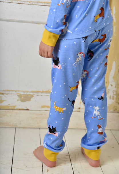Child wearing blue pajama set with animal prints on a white floor.. CHILDREN'S CAT & DOG PRINT COSY COTTON KNIT PYJAMAS | POWELL CRAFT