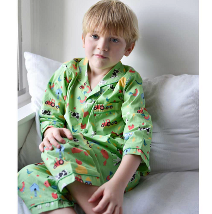 Child wearing green pajamas with colorful patterns sitting on a couch. CHILDREN'S CLASSIC BUTTON UP FARMYARD PYJAMAS | POWELL CRAFT