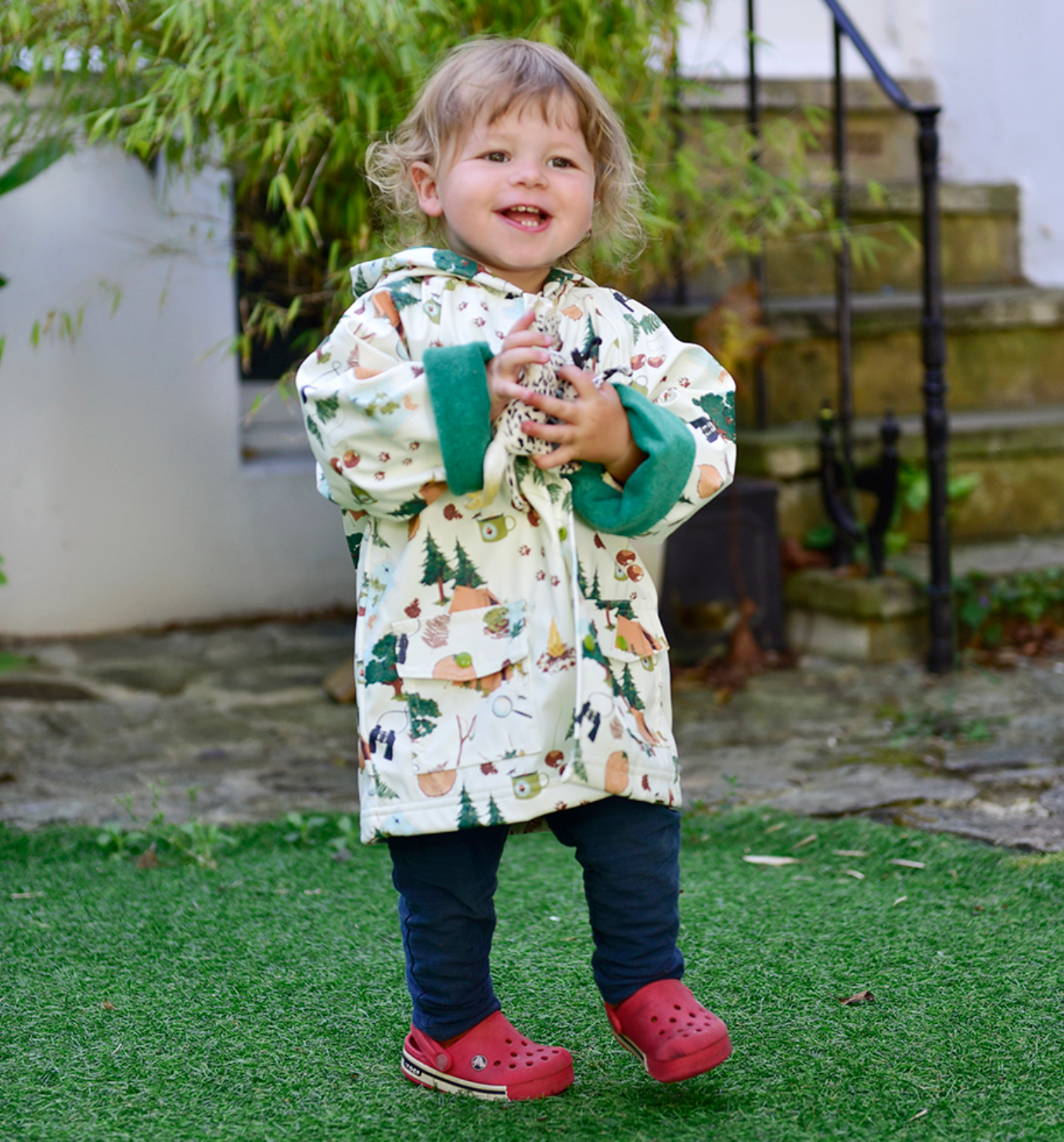 Child wearing a patterned raincoat with red shoes outdoors. CHILDREN'S GREAT OUTDOORS RAINCOAT - 3 SIZES | POWELL CRAFT