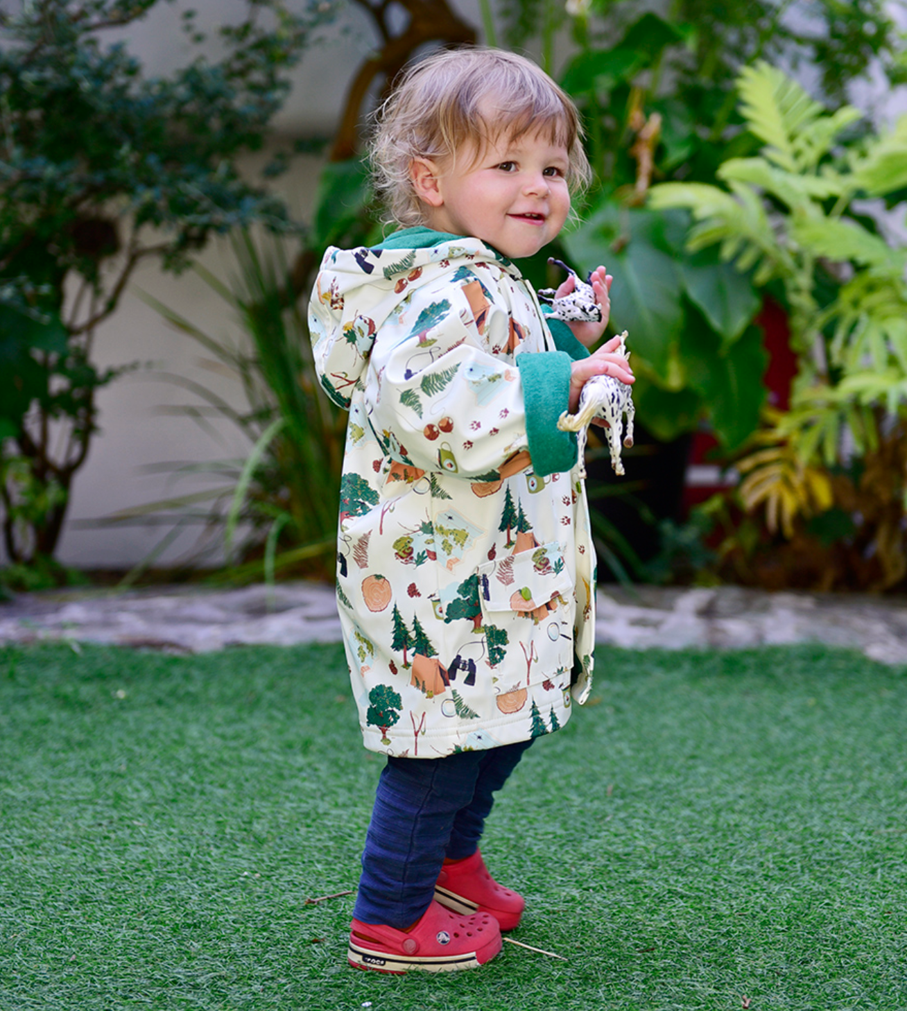Child wearing a patterned coat standing on grass with plants in the background. CHILDREN'S GREAT OUTDOORS RAINCOAT - 3 SIZES | POWELL CRAFT