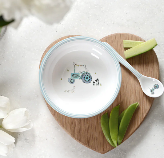 Ceramic bowl with tractor design on a wooden board with a spoon and green leaves. CHILDREN'S MELAMINE BABY SPOON - ON THE FARM | SOPHIE ALLPORT