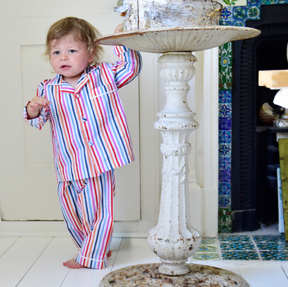 Child in colorful pajamas standing next to a decorative table in a room with a fireplace. CHILDREN'S MULTI-COLOURED STRIPE PYJAMAS | POWELL CRAFT