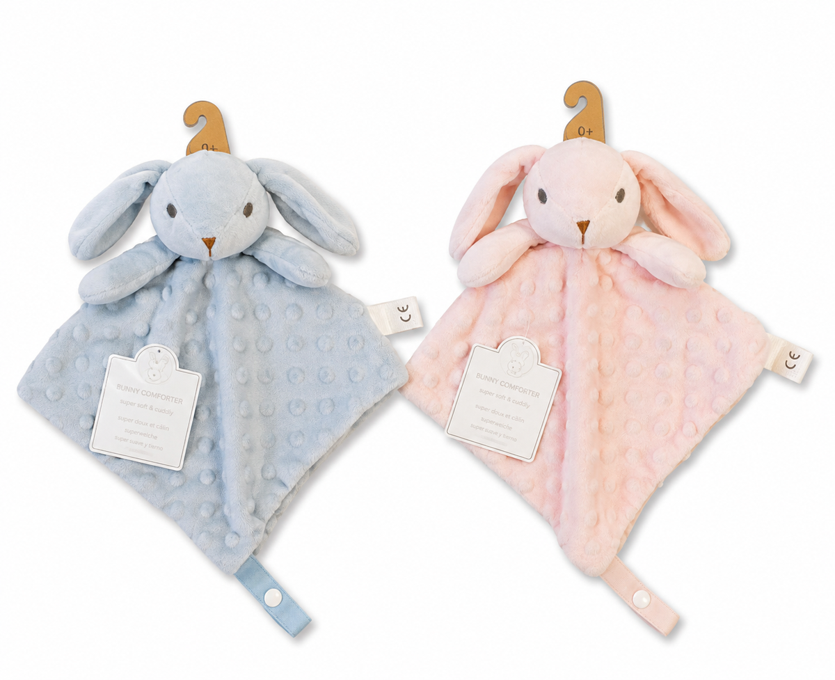 Both-colourway product image — blue left, pink right; 3D plush bunny head with long floppy ears, embroidered dot eyes and brown nose, small plush arms/paws; bubble dot minky blanket body in each colour; satin ribbon loop with press stud at bottom point; CE label in right seam; scalloped Snuggle Baby hang tag; wooden 0+ hanger tag at top of each.